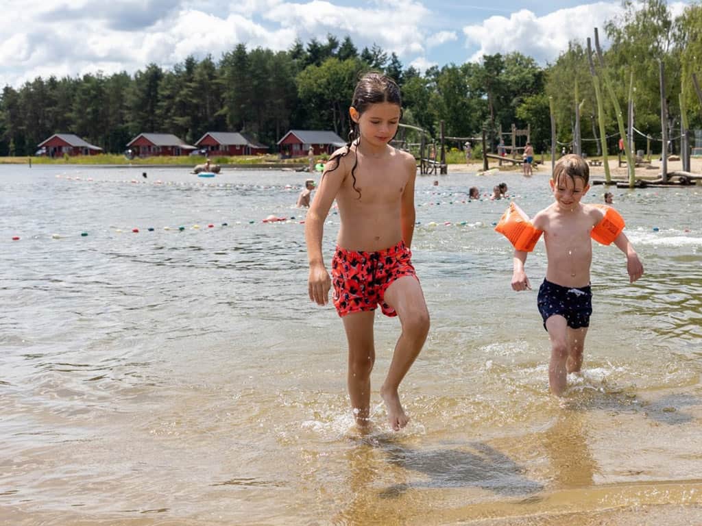 Impressie van de recreatieplas met op de achtergrond enkele huisjes op vakantiepark en camping de Flaasbloem in Noord-Brabant